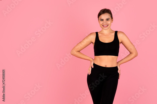 Smiling woman in sportswear with hands on hips posing on pink background