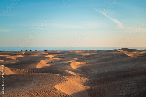 Panoramic landscape of the dunes of a desert at sunset, with the sea in the background. Maspalomas Dunes, Gran Canaria.