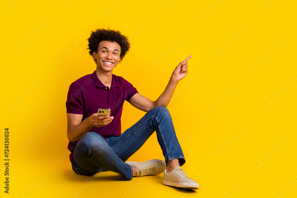 Photo of funny cheerful man wearing stylish violet clothes sitting floor presenting offer discount isolated on yellow color background Photo of funny cheerful man wearing stylish violet clothes sitting floor presenting offer discount isolated on yellow color background