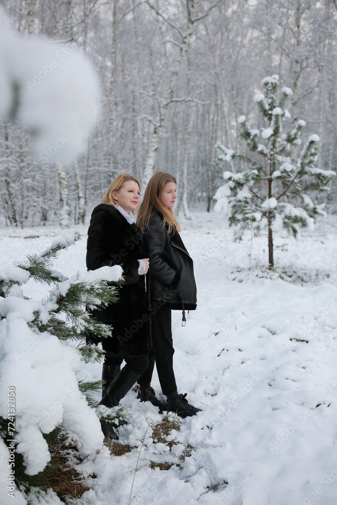 mother and daughter in a snowy forest. a woman in a fur black fur coat in winter in the forest. middle-aged woman winter photo session with her daughter mother and daughter in a snowy forest. a woman in a fur black fur coat in winter in the forest. middle-aged woman winter photo session with her daughter