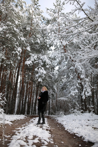 beautiful forty-year-old woman in a snowy forest. a woman in a fur black fur coat in winter in the forest. middle-aged woman near snowy trees