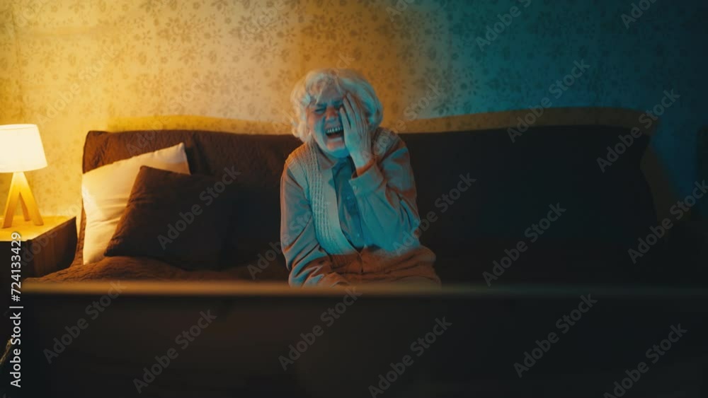 Happy old woman watching a night comedy show on TV and laughing, sitting on sofa Happy old woman watching a night comedy show on TV and laughing, sitting on sofa