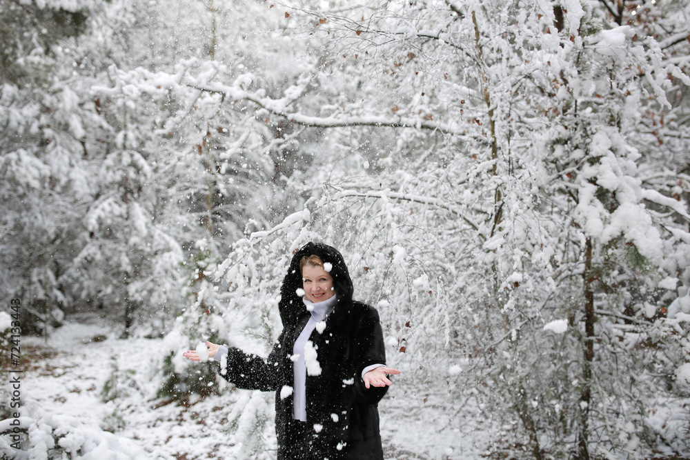 beautiful forty-year-old woman in a snowy forest. a woman in a fur black fur coat in winter in the forest. middle-aged woman near snowy trees