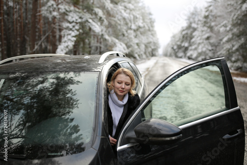beautiful forty-year-old woman in a snowy forest. a woman in a fur black fur coat stands near a black car in winter in the forest. middle-aged woman and a car