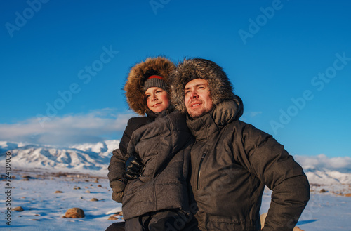 Portrait of happy father and son in hooded winter jackets on mountains background