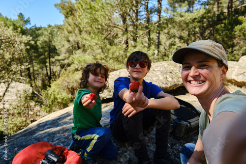Cheerful family taking a selfie and enjoying their vacation sitting on a shady rock in the forest. © roberjzm