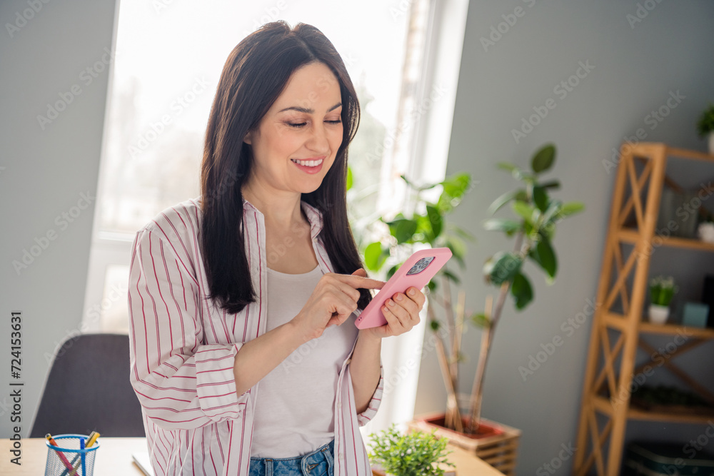 Photo of positive gorgeous lady beaming smile use smart phone communicate social network modern interior office indoors Photo of positive gorgeous lady beaming smile use smart phone communicate social network modern interior office indoors