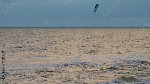 Obraz na płótnie Kitesurfing. Kiteserferzy o zachodzie słońca na tle złocistego morza. Silny wiatr tworzy doskonałe warunki do powietrznych ewolucji. Pastelowe kolory, low key. w salonie