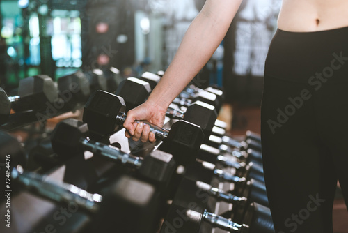 Close up of Confident muscular Asian athlete female is lifting a dumbbell in gym or fitness to build up her body and muscle. Wellbeing  wellness of city people lifestyle  Serious and effort work out.