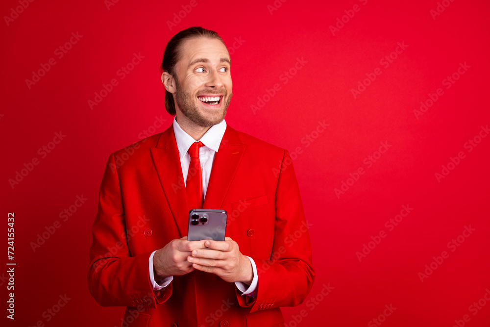 Photo portrait of attractive young man hold telephone look empty space wear trendy classic clothes isolated on red color background Photo portrait of attractive young man hold telephone look empty space wear trendy classic clothes isolated on red color background