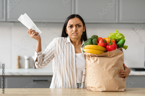 Unhappy young indian woman with grocery bag and receipt