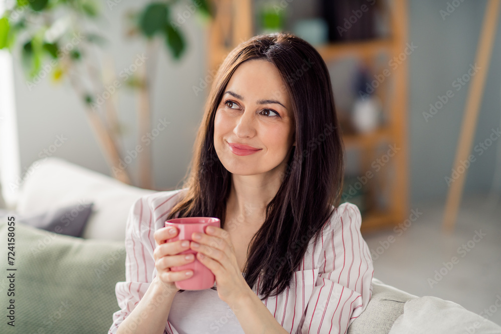 Photo of minded lovely lady sitting couch hands hold cacao mug look curious away contemplate fantasize house indoors Photo of minded lovely lady sitting couch hands hold cacao mug look curious away contemplate fantasize house indoors