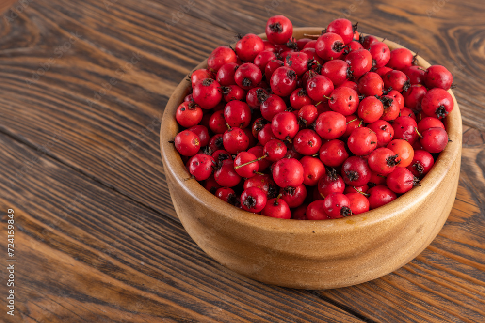 red hawthorn berries in wooden bowl on flat wooden surface. red hawthorn berries in wooden bowl on flat wooden surface.