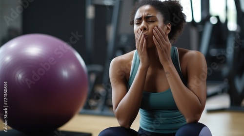 A woman is pictured sitting on a yoga ball in a gym. This image can be used to promote fitness, exercise, and healthy lifestyle concepts