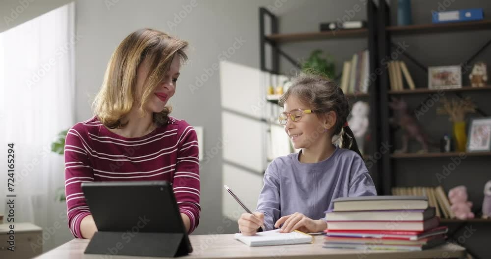 Happy family. Mother helping daughter doing homework at home desk. Mother and daughter together studying online with digital tablet. Children remote education
