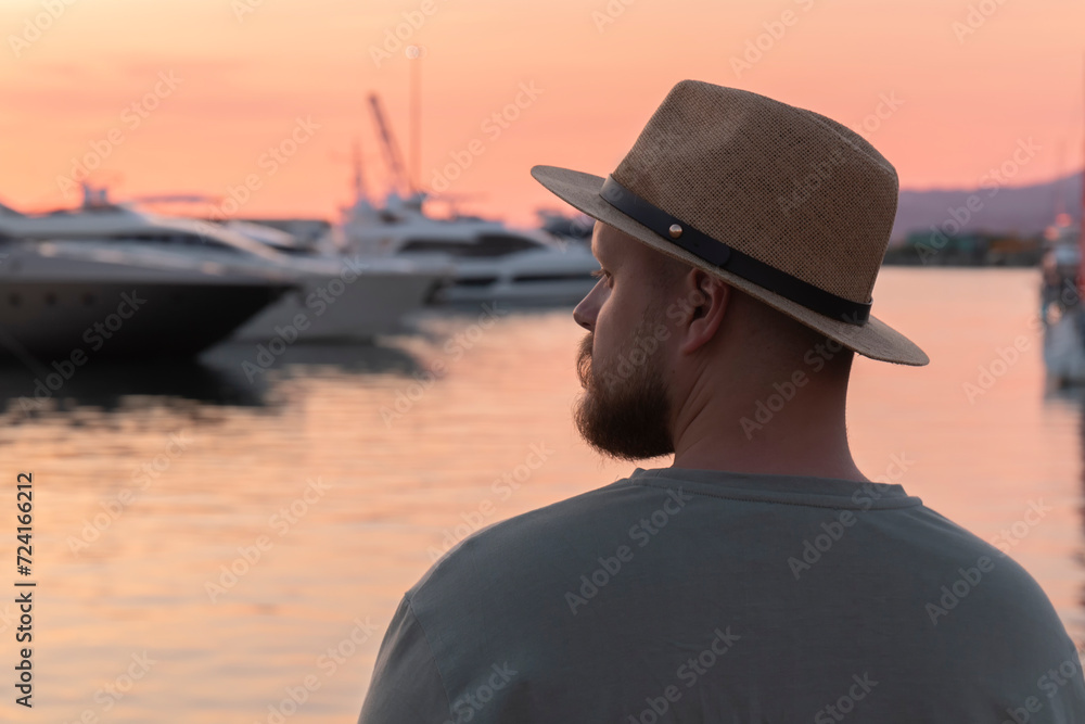 Male against the background of yachts and boats moored at the seaport and colorful sunset. The seaport of Sochi.