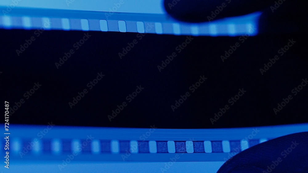 Silhouette of film in a man's hand on blue background close up. Texture of old film, easy to use in composition.