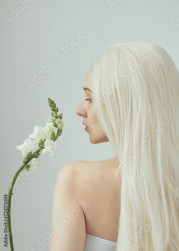 Canvas Print a woman with white hair on a light background holds a white flower in her hand