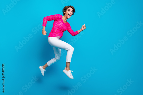 Full length photo of cheerful positive woman wear knitted neon shirt jumping high running empty space isolated blue color background