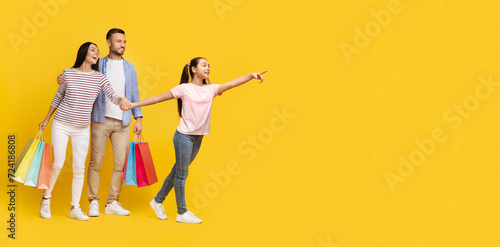Family Shopping. Happy Parents And Daughter Holding Shopper Bags And Pointing Aside