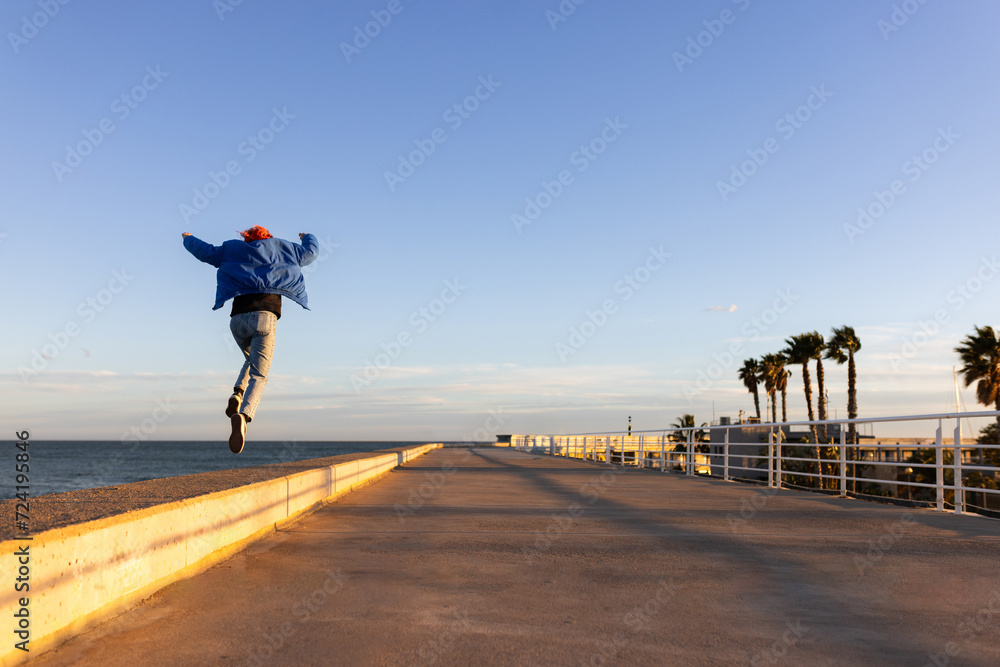 woman dancing in a port at sunset, red hair, smiling - obrazy, fototapety, plakaty 