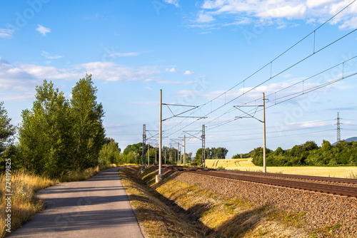 A narrow asphalt road running along an electrified railway line.