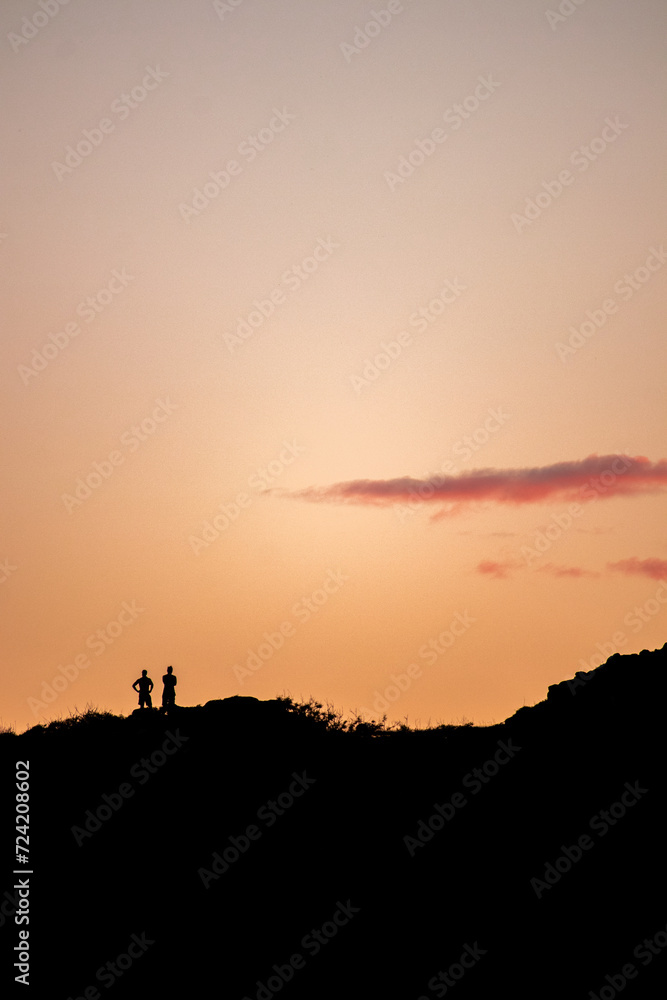 Silhouette of two people watching the sunset on top of a hill in O'ahu, Hawaii