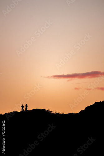 Silhouette of two people watching the sunset on top of a hill in O'ahu, Hawaii © Wirestock