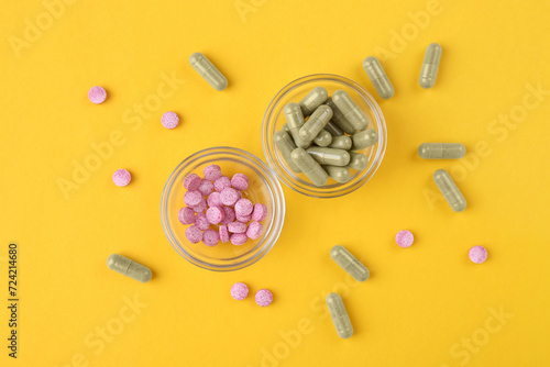 Different vitamin pills in glass bowls on yellow background, flat lay
