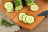 Cucumbers, knife, cutting board and dill on wooden table, flat lay