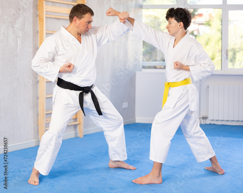 Active teen male karate practitioner training battling methods with middle-aged partner in sports hall