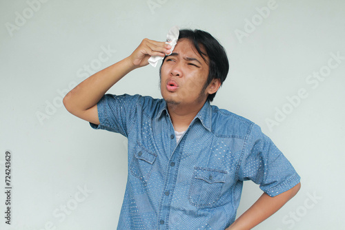 Close up portrait of Asian young man in blue shirt with het gestures in the summer and wiping sweat with tissue. photo