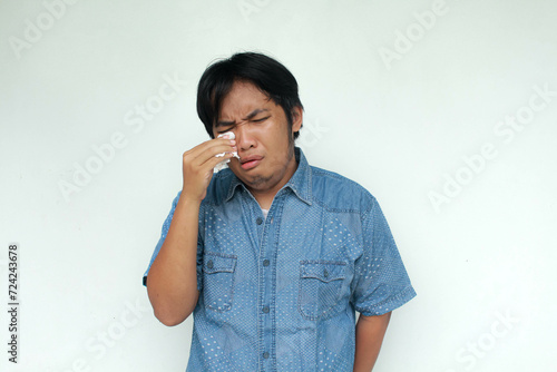 Obraz na płótnie Crying face of Asian man with hand holding tissue isolated on gray background