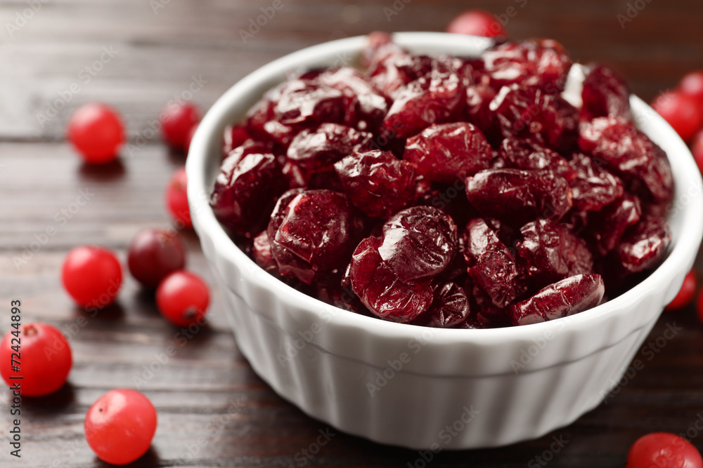 Tasty dried cranberries in bowl and fresh ones on wooden table, closeup Tasty dried cranberries in bowl and fresh ones on wooden table, closeup
