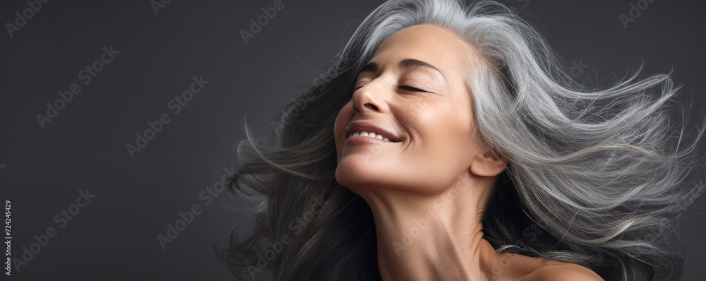 A gorgeous happy smiling senior woman with closed eyes and long grey hair over a grey background A gorgeous happy smiling senior woman with closed eyes and long grey hair over a grey background