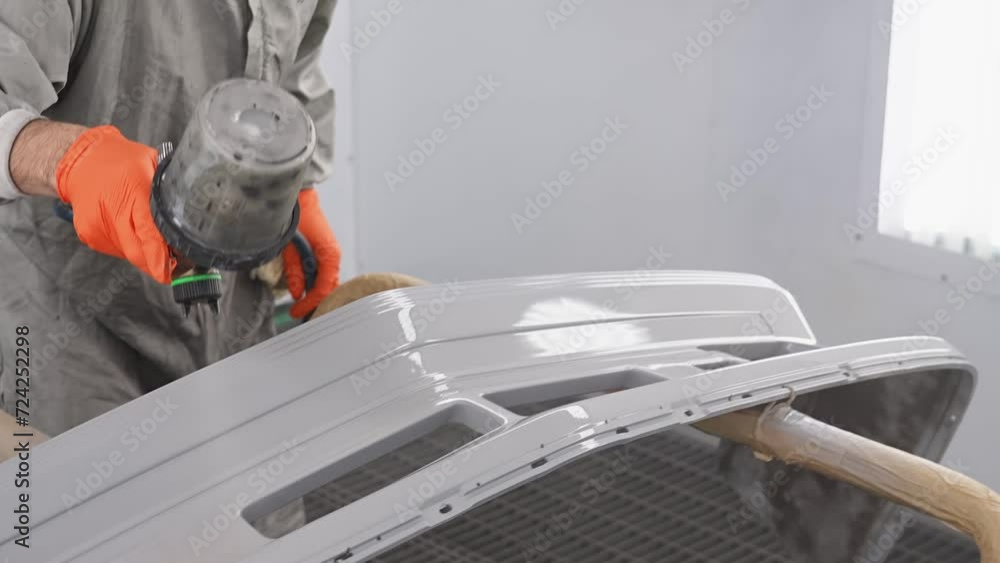 Modern car painting. Man is using spraying machine, holding it in hand, dressed in protective uniform. Master is painting part of automobile in car service. Modern car painting. Man is using spraying machine, holding it in hand, dressed in protective uniform. Master is painting part of automobile in car service.