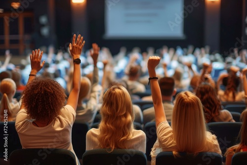 A diverse group of individuals in stylish clothing raise their hands in unison, adding to the electrifying energy of the packed auditorium at a conference hall