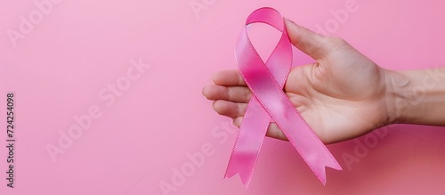 Closeup woman hand holding pink ribbon for breast cancer awareness isolated background. Generated AI