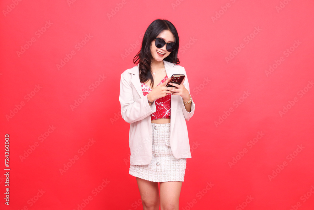 A beautiful Asian Indonesian woman wearing glasses, cheerfully slanted to the left, operates a cellphone cheerfully wearing a cream-colored blazer A beautiful Asian Indonesian woman wearing glasses, cheerfully slanted to the left, operates a cellphone cheerfully wearing a cream-colored blazer