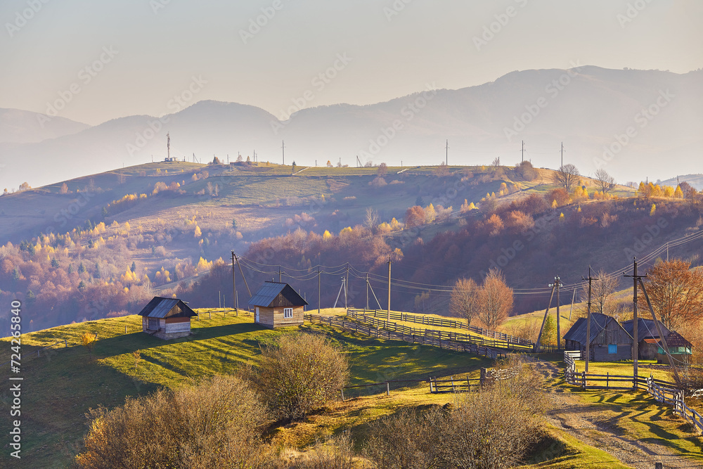 Panoramic view of misty sunny autumn evening in mountains. Beautiful sunset hills landscape. Slopes, meadows, fields, village, house, dirt road. Amazing fall rural scene. Carpathian range.