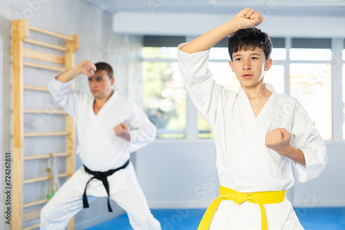 Adult man and boy teen karatekas train karate technique in studio