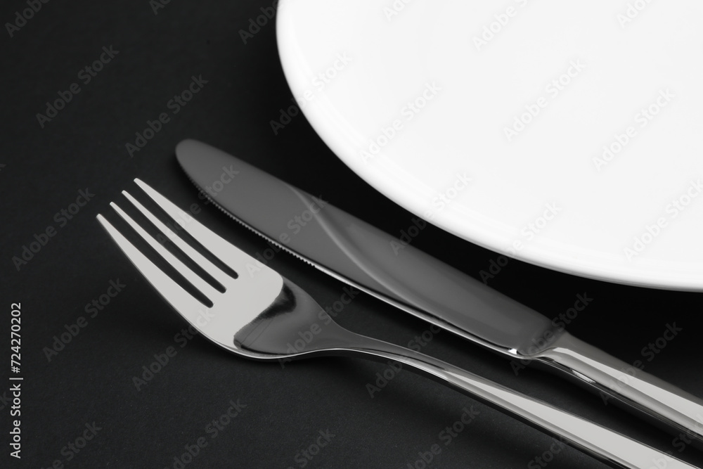 Clean plate, fork and knife on black table, closeup