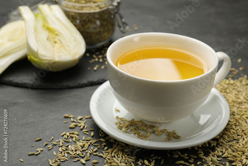 Aromatic fennel tea in cup and seeds on black table, closeup. Space for text