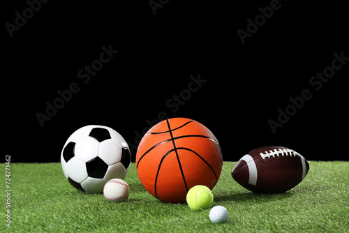 Many different sports balls on green grass against black background, space for text