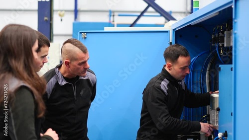 Young employee teaching coworkers how to use an industrial machine. Educational training class in a factory.