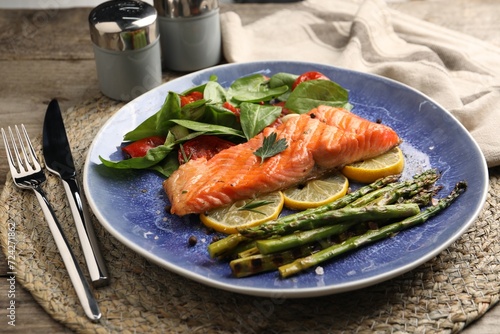 Tasty grilled salmon with tomatoes, asparagus, spinach and lemon served on table, closeup