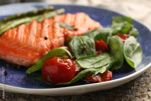 Tasty grilled salmon with tomatoes, spinach and spices on table, closeup