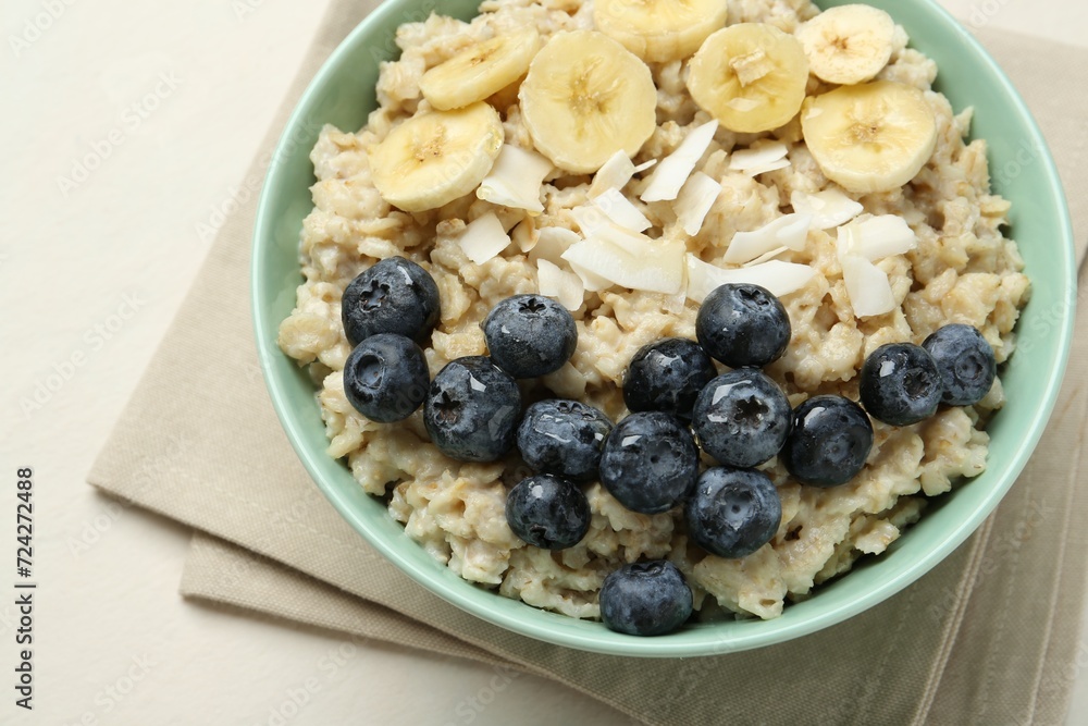 Tasty oatmeal with banana, blueberries, coconut flakes and honey served in bowl on beige table, closeup Tasty oatmeal with banana, blueberries, coconut flakes and honey served in bowl on beige table, closeup