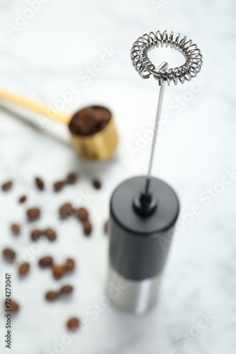 Black milk frother wand and coffee beans on white marble table