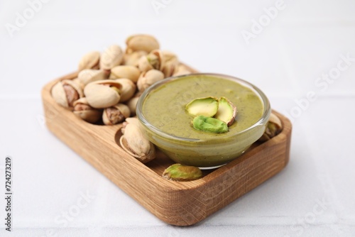 Tasty pistachio cream in bowl and nuts on white tiled table, closeup